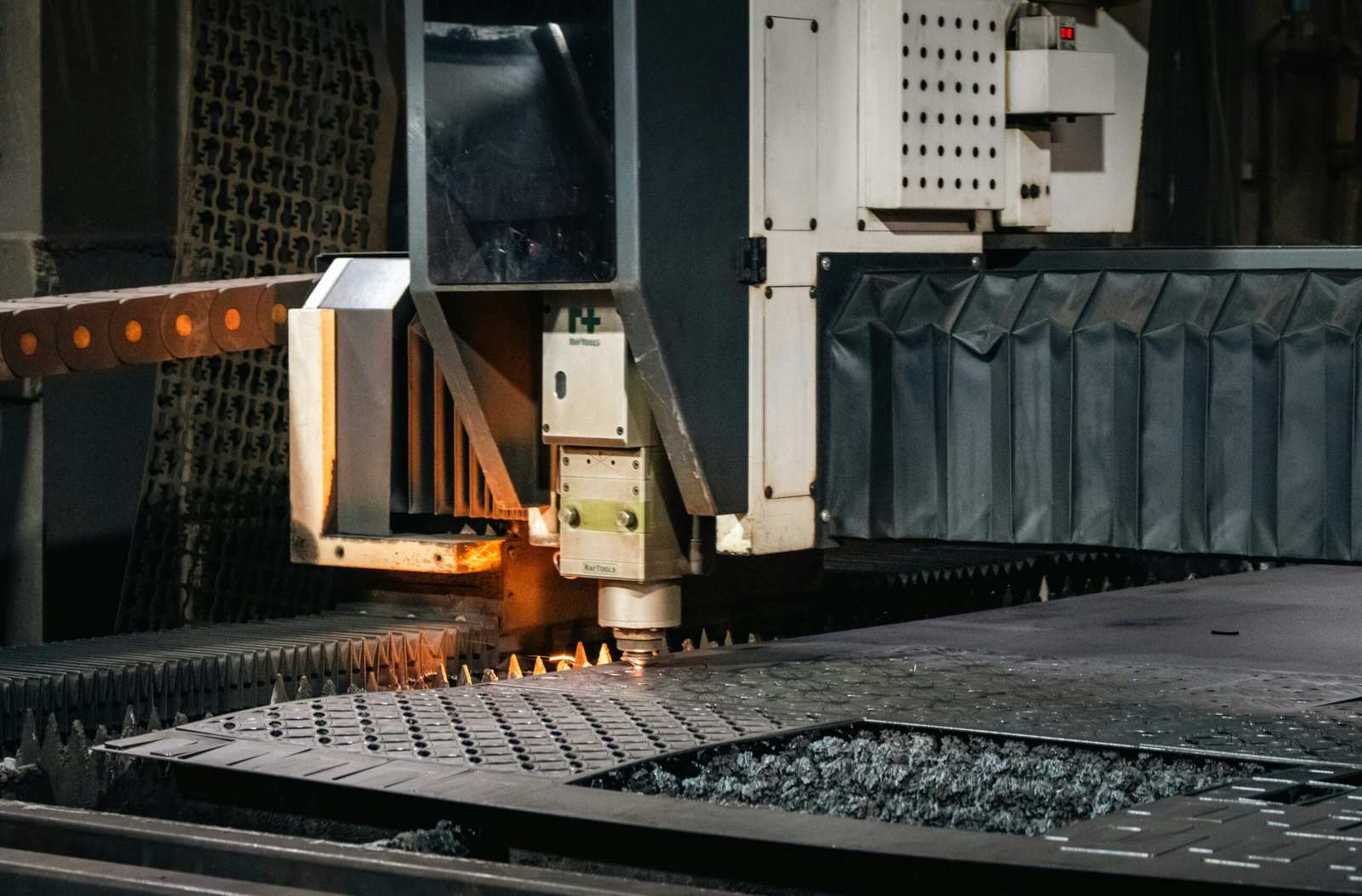 Close-up of a CNC laser cutting head cutting metal on a spiked bed